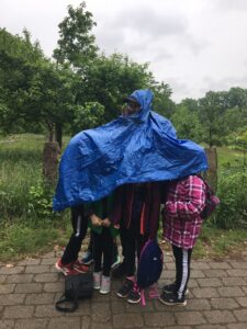Kinder stehen unter einer Plane um sich vor Regen zu schützen
