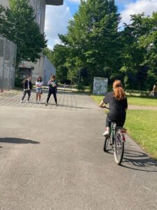 Schüler stehen auf Sportplatz, eine Schülerin fährt Fahrrad