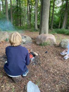Gut Basthorst - Junge sitzt mit Hinteransicht im Wald am Lagerfeuer