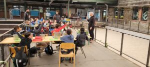 Kinder sitzen in der Alten Gleishalle und hören dem Koch zu