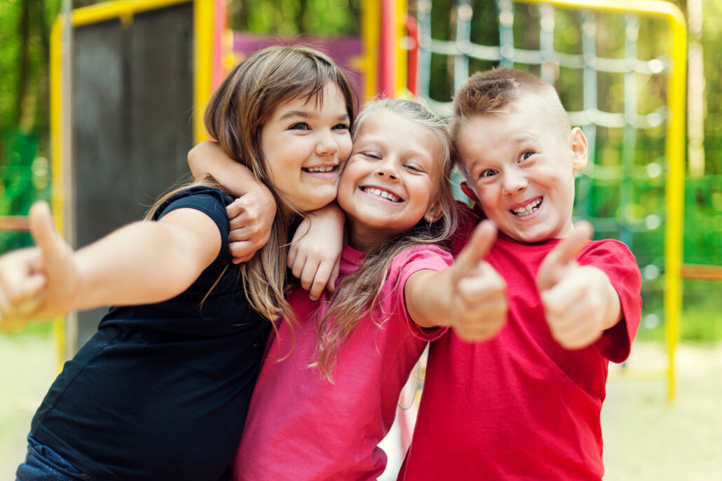 glueckliche kinder die ok zeichen auf spielplatz zeigen